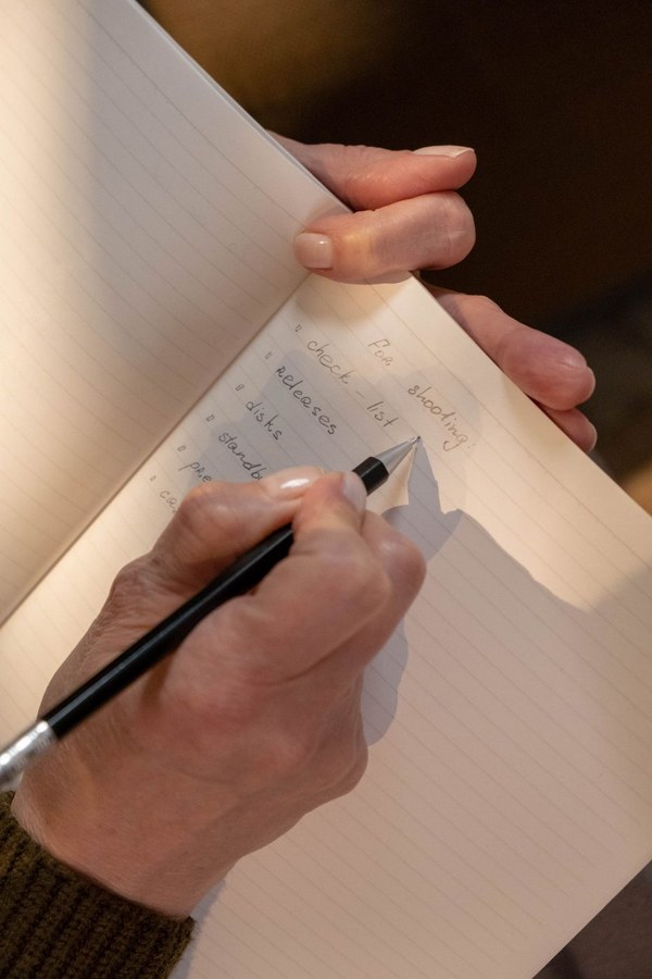 A writer's hands on an open Muji notebook, morning light on wooden table.