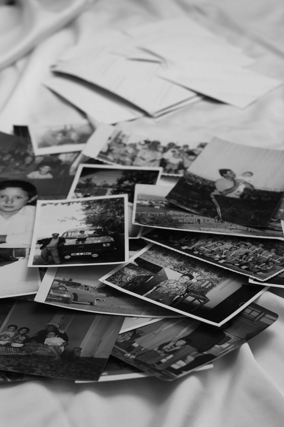A collection of black-and-white photographs scattered on white fabric, some showing 1960s Singapore.